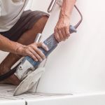Yacht maintenance. A man polishing side of the white boat by grinder machine in the marina