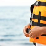 Male lifeguard putting on life vest near sea, closeup